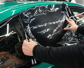 Applying tinting foil on a car window in the tuning studio close-up. Male car service worker glue...