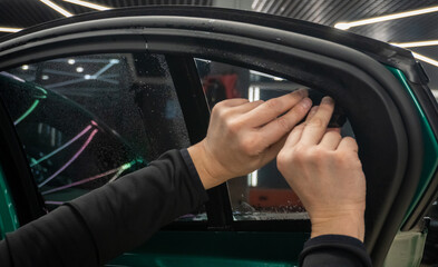 Applying tinting foil on a car window in the tuning studio close-up. Male car service worker glue...