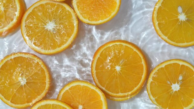 Close up video of mandarin slices surrounded by water ripples. White background with half oranges placed on water waves.