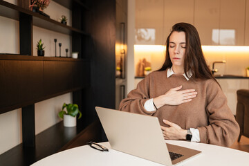 Woman meditating while sitting in front of her laptop in living room
