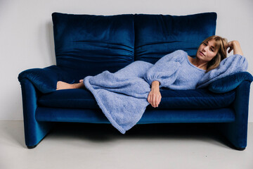 Obraz premium Woman in a blue knit dress relaxing on a stylish blue sofa.