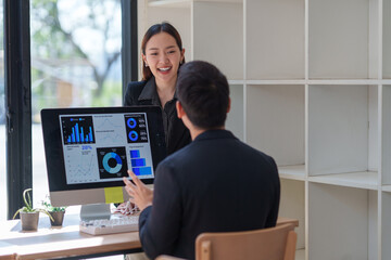 Two asian businesspeople are discussing business performance using charts and data displayed on a...