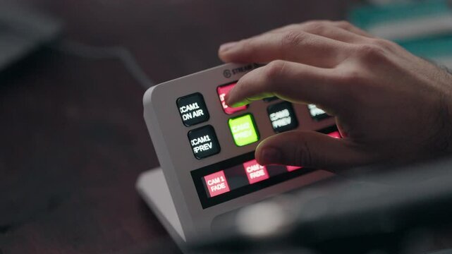 Close up of a hand operating a live stream switcher with illuminated buttons for video control