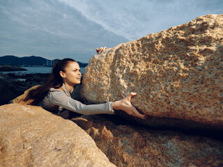 A determined young woman in activewear, climbing rock formations during an overcast day,...