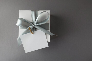 Gray gift box with satin ribbon and blank sticker on gray background, top view