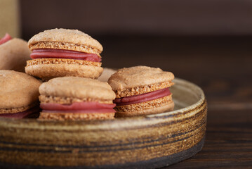 Vegan homemade caramel macarons with raspberry cream on shea butter in a plate on a wooden table, closeup. Sugar, lactose and gluten free.