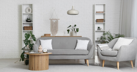 Interior of light living room with grey sofa, armchair and table with plants