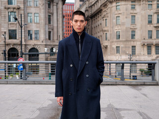 Portrait of handsome Chinese young man wearing black overcoat posing in the street, young guy with...