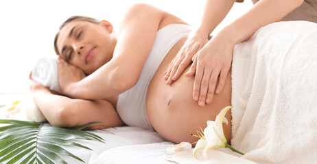 Obraz premium Young pregnant woman having massage on couch in spa salon