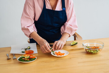 A woman is chopping cucumbers while surrounded by colorful vegetables in a cozy kitchen