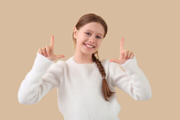 Little girl pointing at something on beige background