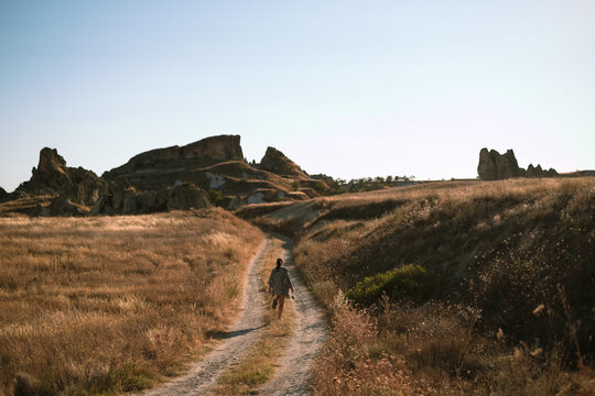 Woman Walks Through Golden Fields and Rocky Terrain in Cappadocia