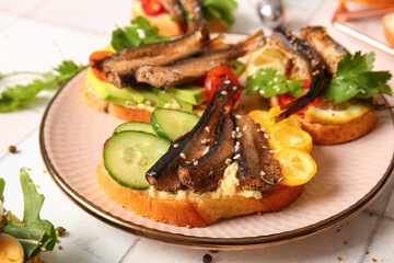 Plate of tasty sandwiches with canned smoked sprats on table