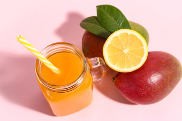 Mason jar of fresh mango smoothie and lemon on pink background, closeup