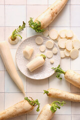 Plate with fresh daikon radishes on white tile background