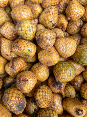 A close-up of Atapson or Asam Paya a fruit from Kalimantan Indonesia with scaly, golden-brown skin and a glossy texture, piled together at a traditional market.