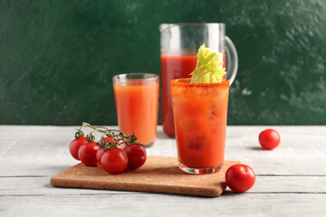 Glasses and jug of bloody mary with celery on green wooden table