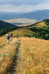 A group of tourists trekking downhill through golden fields and forested hills in Armenia during autumn, experiencing stunning landscapes and adventure hiking in fall colors