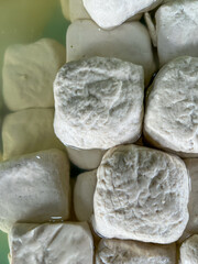 A close-up of fresh tofu cubes soaking in water, showing their soft, textured surfaces and pale color. It is sale on the traditional market.