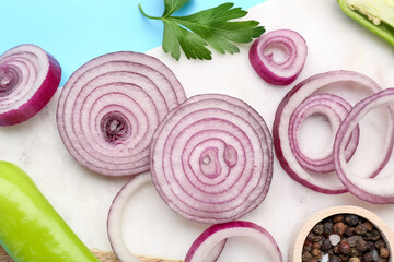 Board with fresh onion slices, jalapeno and spices on blue background, closeup