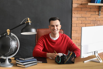 Male teacher writing at table in classroom