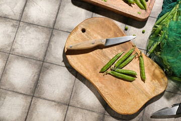 Wooden cutting board with green peas on grey tile background