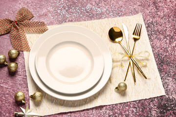 Festive table setting with golden cutlery, Christmas balls and bow decorations on pink background