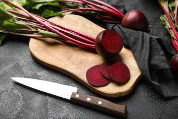 Cutting board with fresh cut beetroots and knife on black table