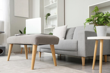 Laptop with newspapers on soft bench in light living room