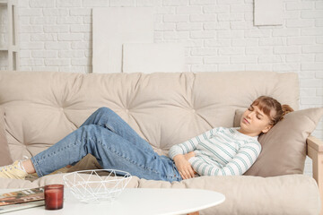 Young woman suffering from stomach ache on sofa at home