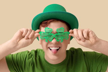 Funny young man in leprechaun's hat with party glasses on beige background. St. Patrick's Day...