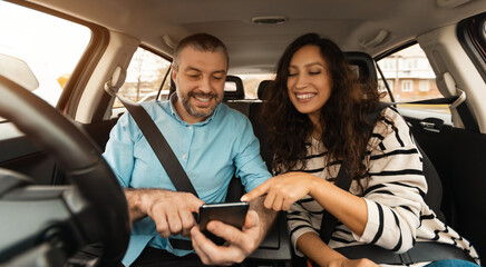 Short Road Route. Portrait of smiling couple sitting inside luxury car pointing fingers at smart...