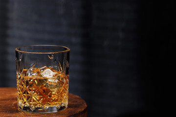 A whiskey glass resting on a wooden table, set against a dark background