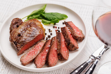 A perfectly cooked sliced striploin steak with a juicy, tender texture, served alongside a glass of rich red wine