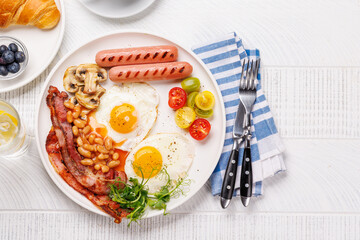 A classic breakfast plate featuring sunny-side-up eggs, crispy bacon, sausages, and fresh tomatoes