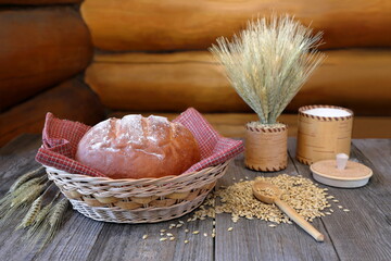 The still life with a loaf of bread and wheat stalks on a log wall background.