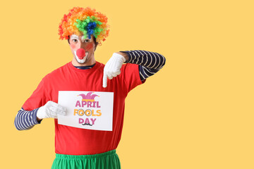 Portrait of clown pointing at poster with text APRIL FOOLS DAY on yellow background