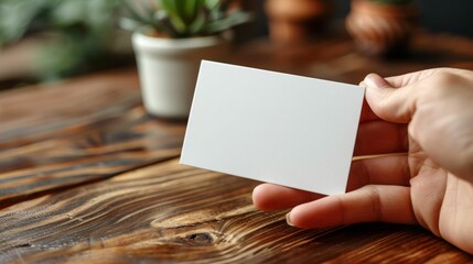 A hand holding a white business card on a wooden table
