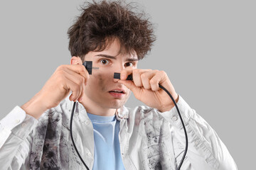 Electrocuted young man with burnt face and plug on light background, closeup