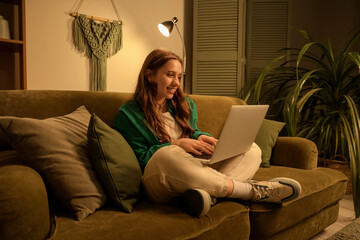 Young woman using laptop on sofa at home in evening
