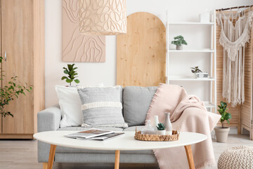 Light interior of stylish living room with sofa, pillows, shelving unit and coffee table