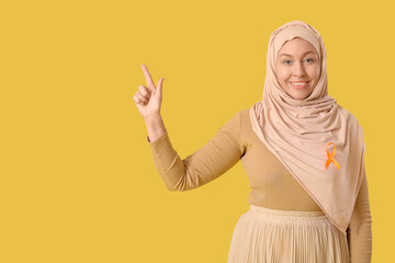 Happy mature Muslim woman with ribbon pointing at something on yellow background. Multiple...