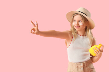 Beautiful girl with bottle of sunscreen cream showing Victory gesture on pink background