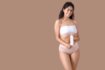 Young African-American woman in menstrual panties with pad on brown background
