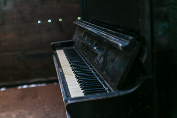 A vintage, upright piano with a distressed, black finish, showcasing its age and character, set against a simple backdrop.