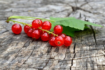 Red currant with green leaves on old wooden background.