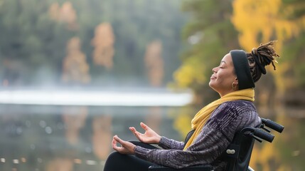 Happy disabled mixed race woman in wheelchair meditating practicing wellness yoga meditation by lake in nature outside
