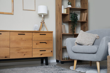 Interior of modern living room with wooden chest of drawers, shelving unit and armchair near beige wall