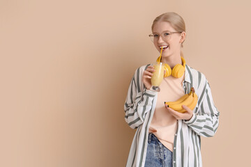 Happy young woman with healthy smoothie and bananas on beige background