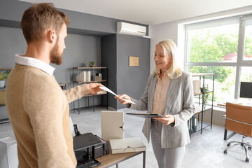 Mature businesswoman with her colleague printing document in office